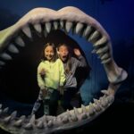 2 girls stood inside the skeleton jaws of a whale shark. One pretends to be scared.