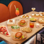 a table with burgers, pizza and nachos